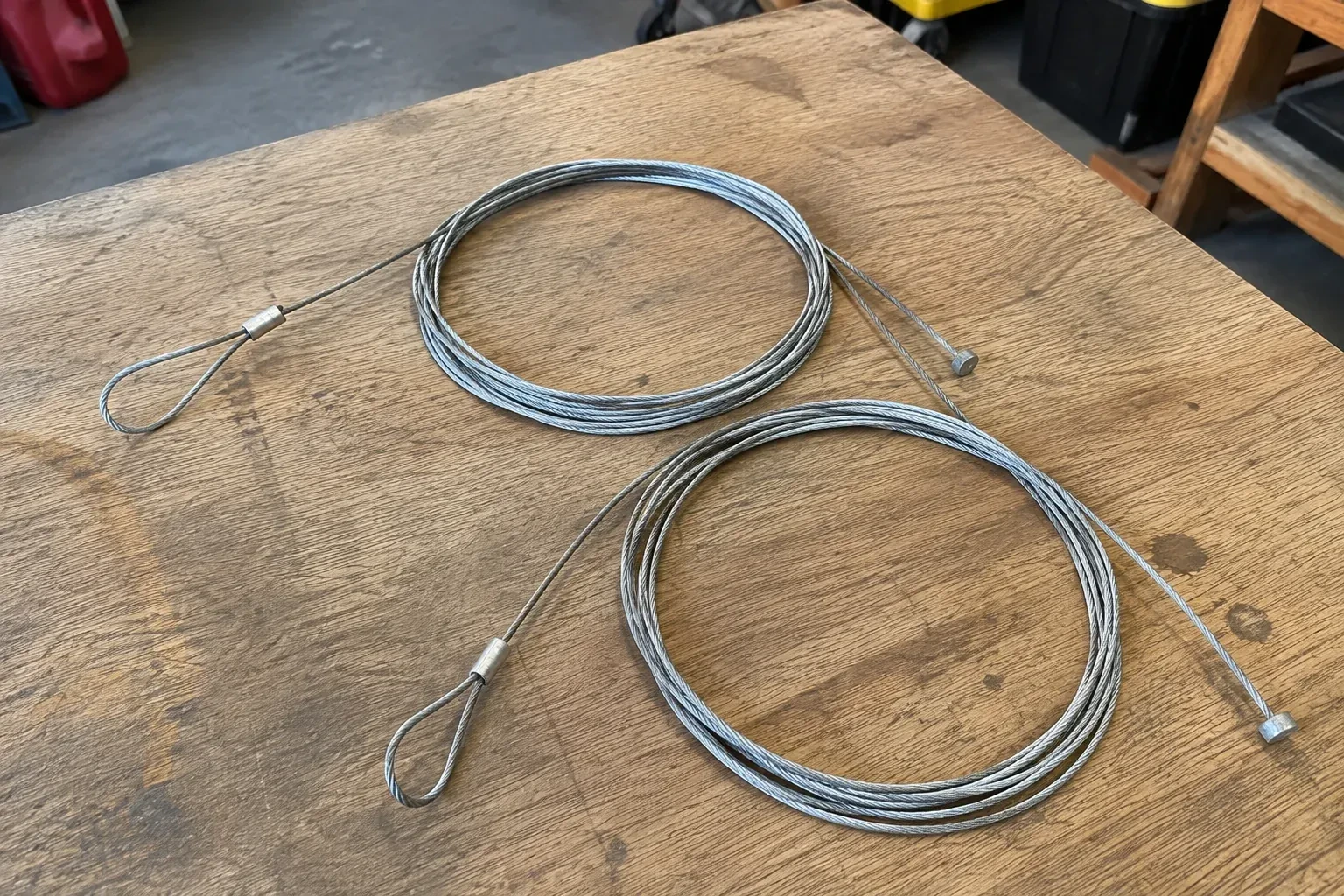 Two coiled steel cables with loop and stop ends on a workbench. — Garage Door Cable Replacement, Fort Erie